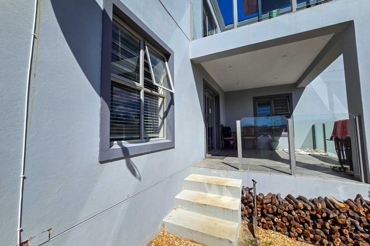Rear exterior view featuring a tiled patio with glass balustrades, concrete steps, and modern casement windows on a light grey rendered facade.