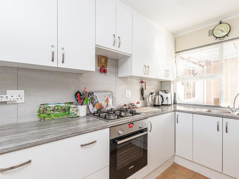 A functional kitchen featuring white cabinetry, grey laminate countertops, a gas hob, built-in oven, and a stainless steel sink with a tiled backsplash.
