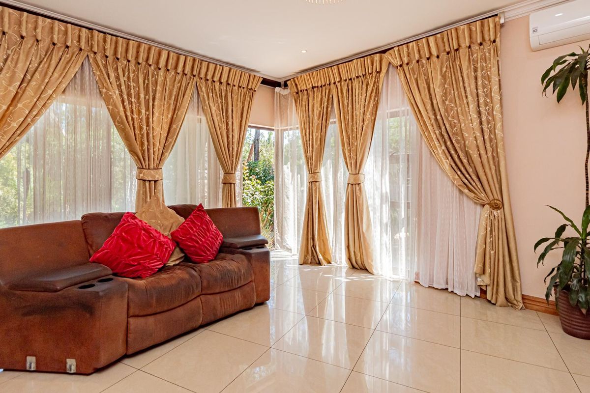 A bright living room featuring large windows with floor-to-ceiling curtains, polished tile flooring, and a wall-mounted air conditioning unit.