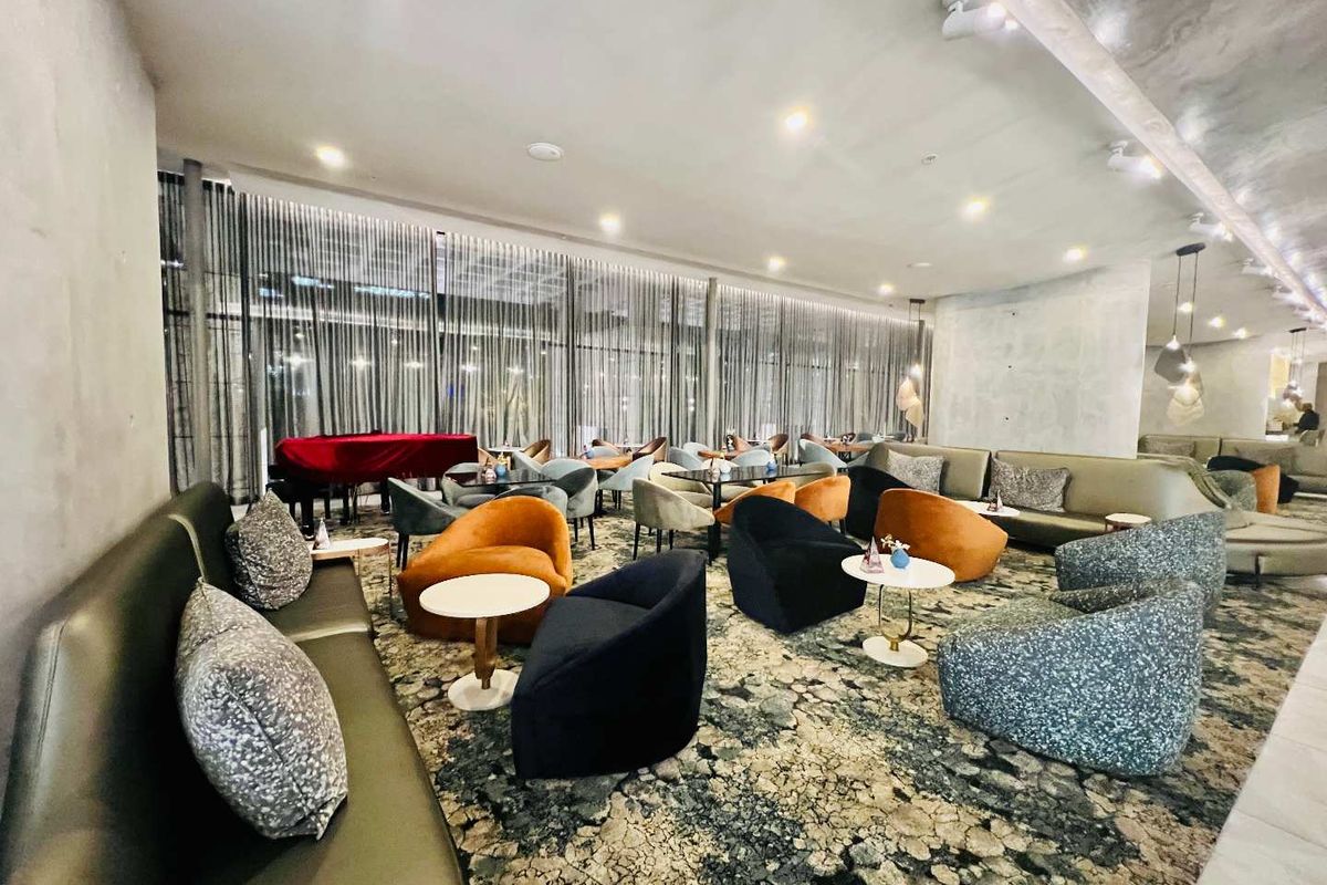 A spacious, modern lounge area featuring floor-to-ceiling windows with sheer curtains, recessed ceiling lighting, and polished concrete-style wall finishes.