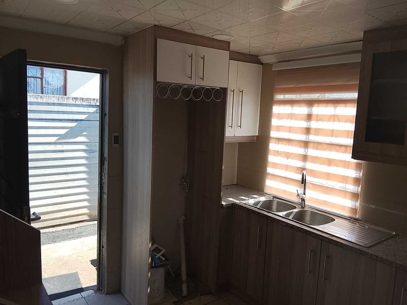A functional kitchen area featuring laminate cabinetry, granite countertops, and a double bowl stainless steel sink with direct access to an exterior space.