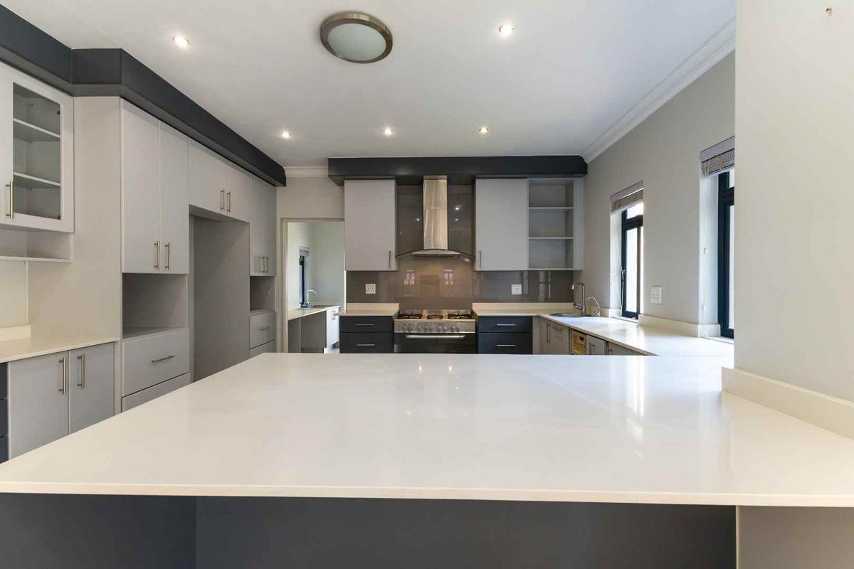 Modern kitchen featuring sleek two-tone cabinetry, quartz countertops, integrated gas hob with extractor, and an adjoining scullery area.