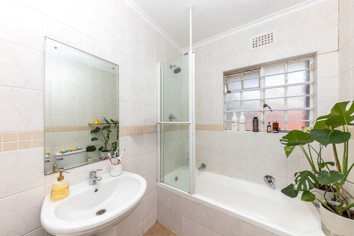 A functional bathroom featuring a pedestal basin, a bathtub with a shower screen, and tiled wall finishes.