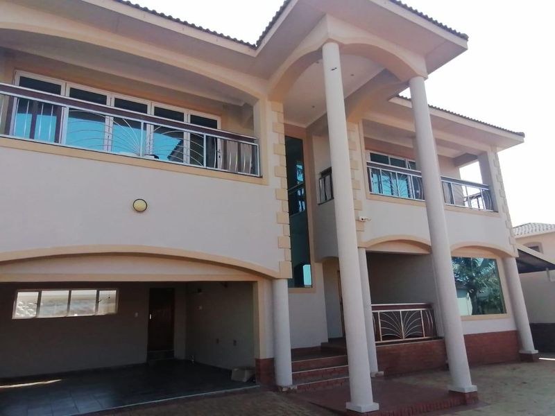 A modern two-story residential facade featuring prominent concrete columns, covered balconies with stainless steel balustrades, and an integrated ground-level garage.