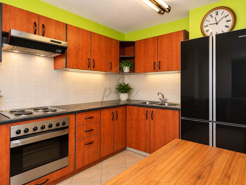 A functional kitchen featuring wood-look laminate cabinetry, dark countertops, a built-in oven with electric cooktop, and a tiled backsplash.