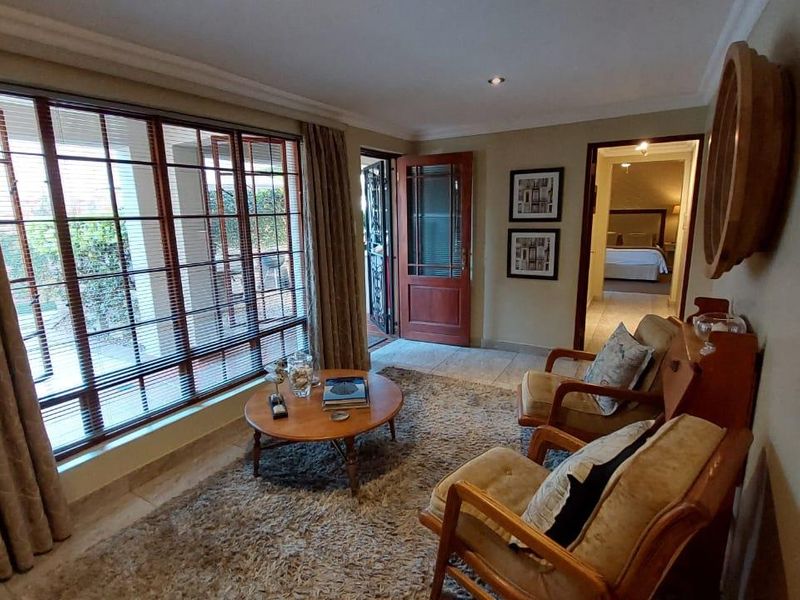 A cozy living room featuring large windows, tiled flooring, and direct access to an outdoor area, with a view into an adjacent bedroom.