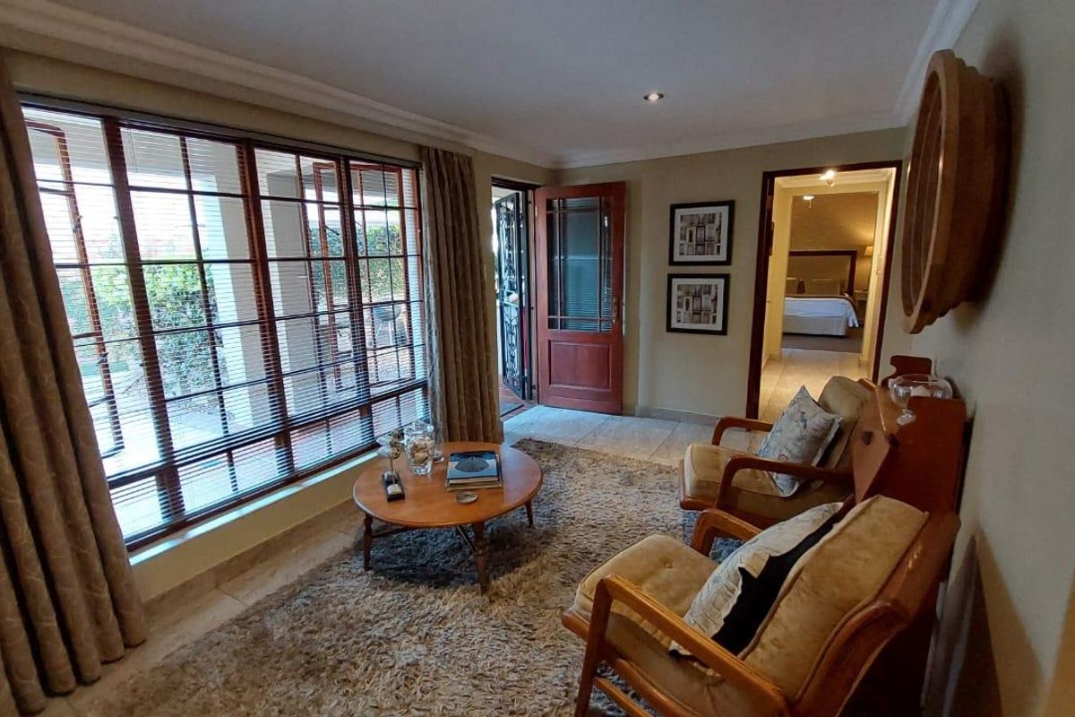 A cozy living room featuring large windows, tiled flooring, and direct access to an outdoor area, with a view into an adjacent bedroom.