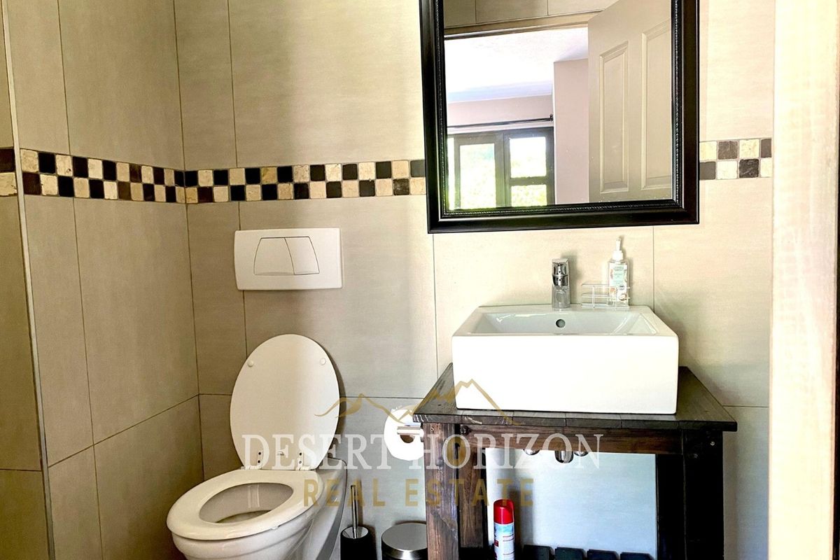 A compact bathroom featuring a wall-mounted toilet, a modern vessel sink on a wooden vanity, and neutral wall tiling with a decorative accent border.
