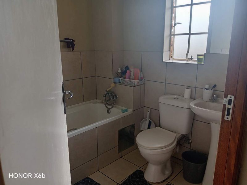 A compact bathroom featuring a bathtub, pedestal basin, and toilet with neutral wall and floor tiling.