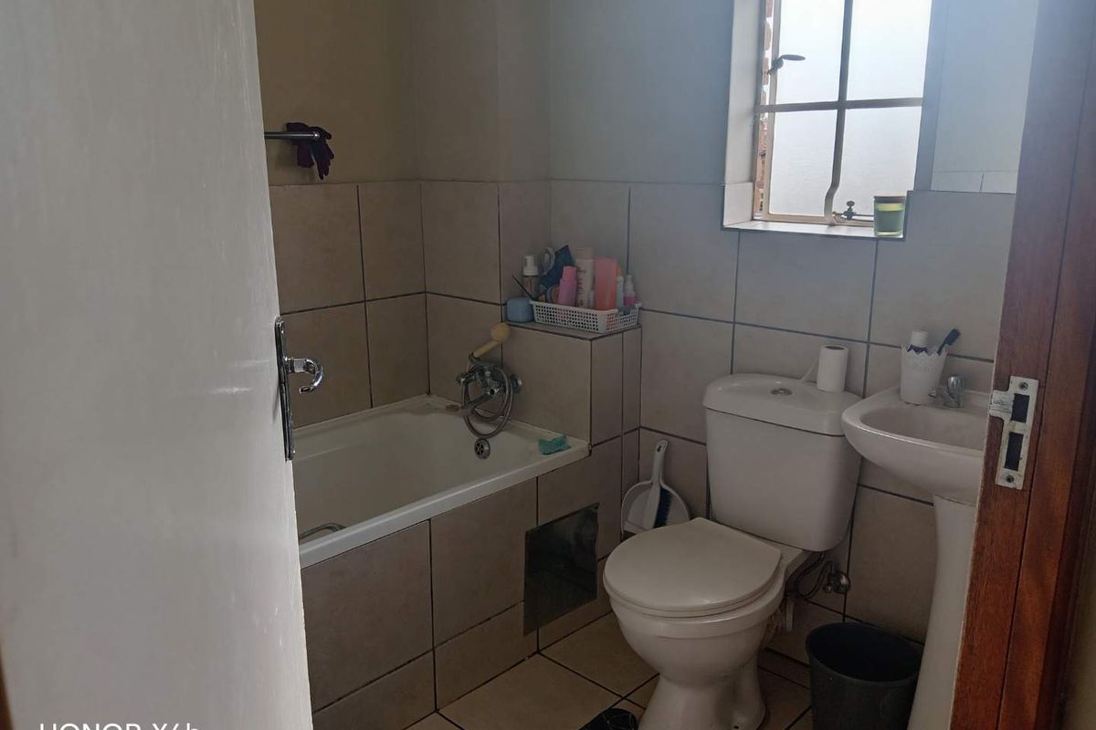 A compact bathroom featuring a bathtub, pedestal basin, and toilet with neutral wall and floor tiling.