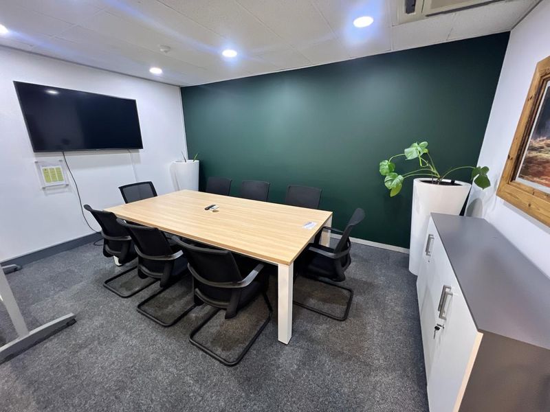 A modern, well-maintained office meeting room featuring a dark green accent wall, recessed ceiling lighting, and professional carpet flooring.
