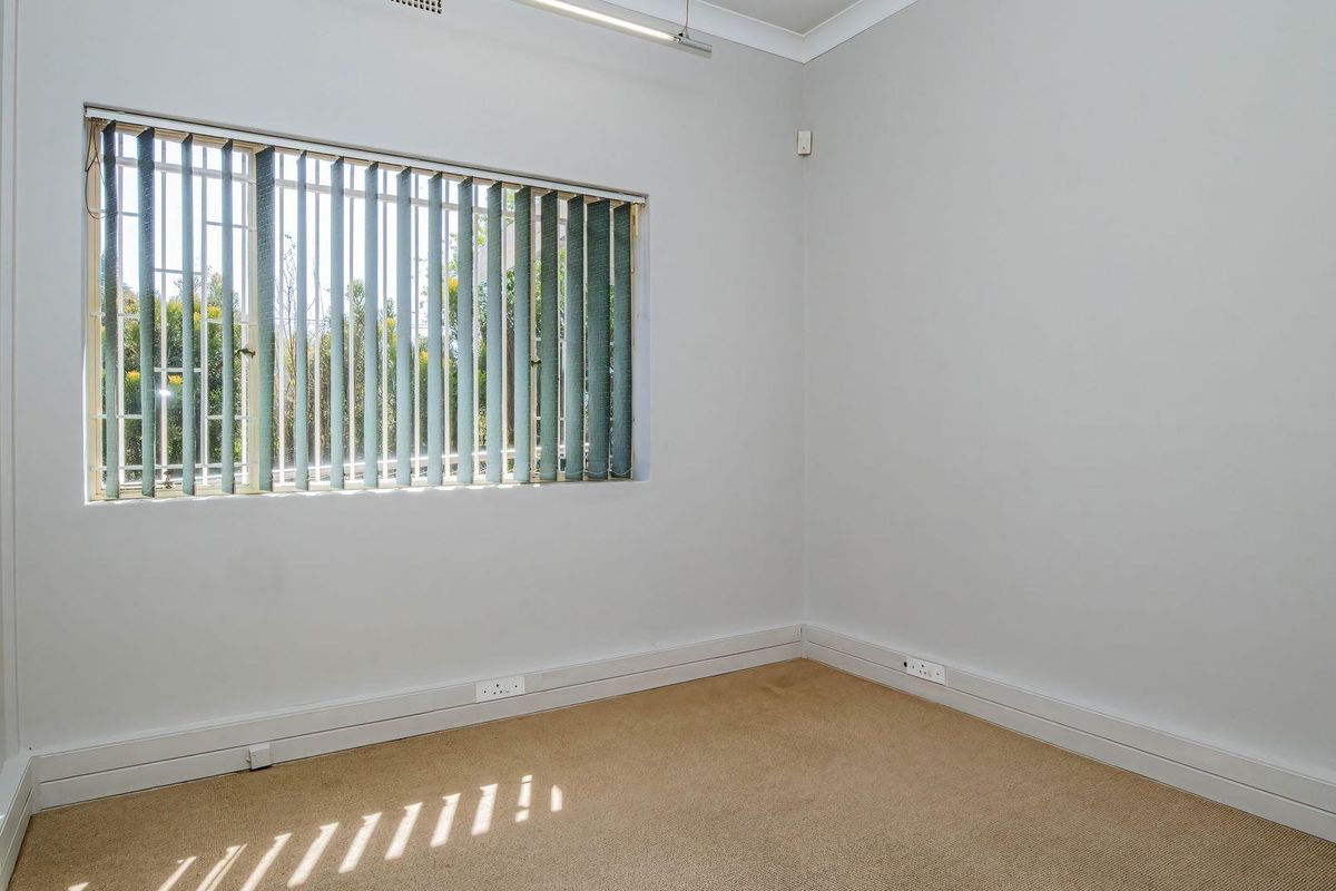 An empty bedroom featuring neutral walls, carpet flooring, and a window fitted with vertical blinds and security bars.