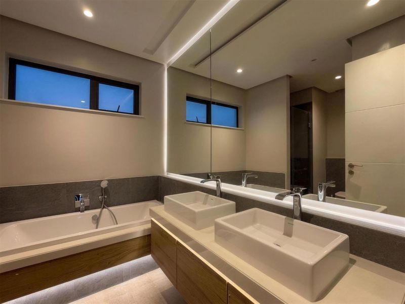 Modern bathroom featuring a double vanity with vessel sinks, a built-in bathtub, and integrated LED lighting with a large mirror.