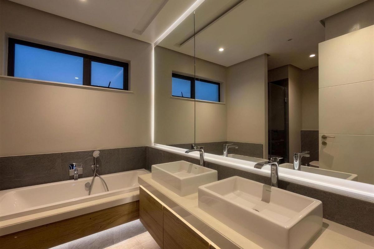 Modern bathroom featuring a double vanity with vessel sinks, a built-in bathtub, and integrated LED lighting with a large mirror.