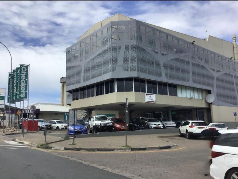 Exterior view of a multi-story commercial office building featuring modern perforated metal cladding and an integrated ground-level parking area.