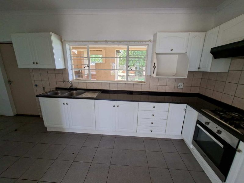 A functional kitchen featuring white cabinetry, dark granite countertops, built-in oven, gas hob, and tiled flooring, offering a clean canvas for potential updates.