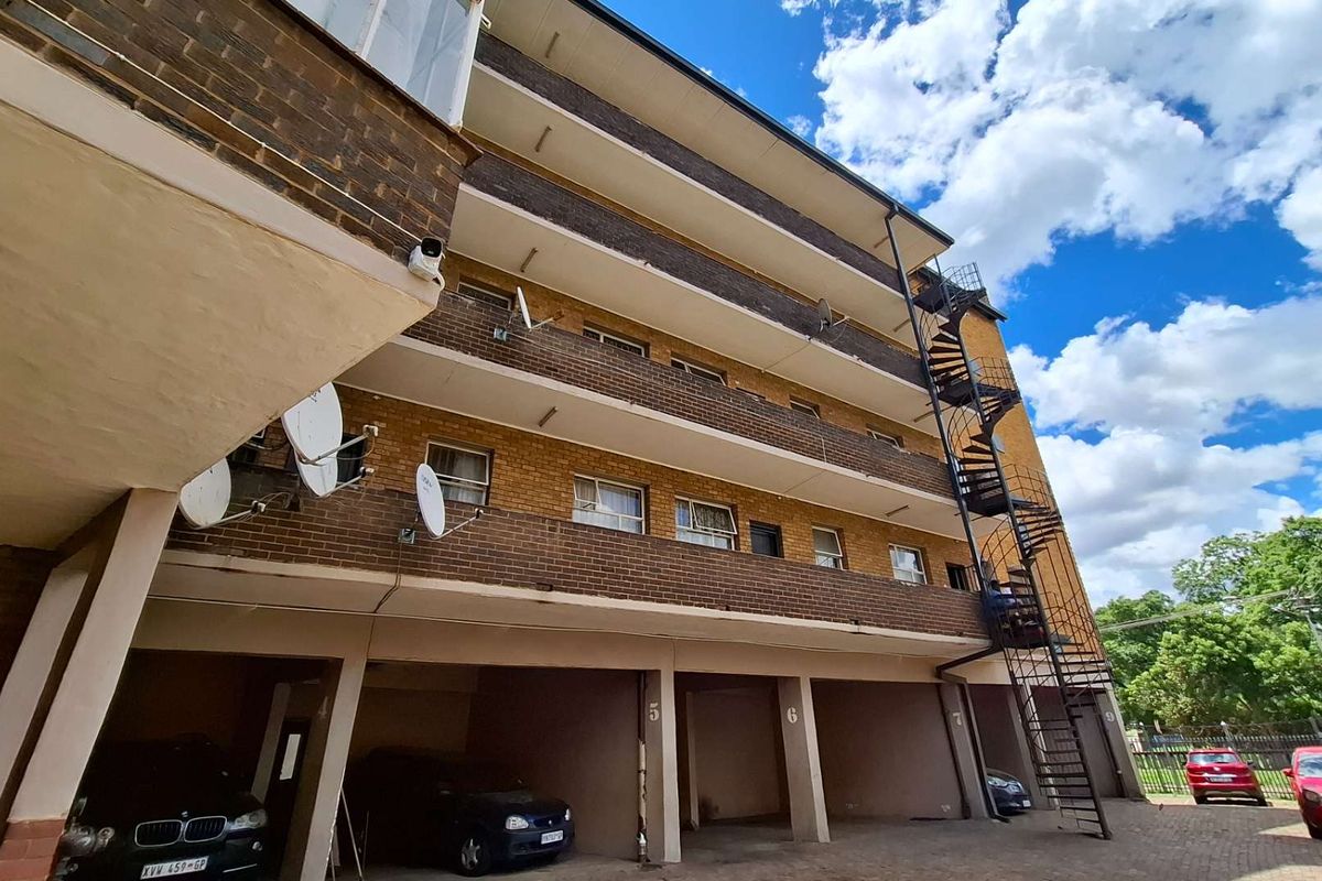 Exterior view of a multi-story apartment building featuring brick facade, covered ground-level parking bays, and an external metal spiral staircase.