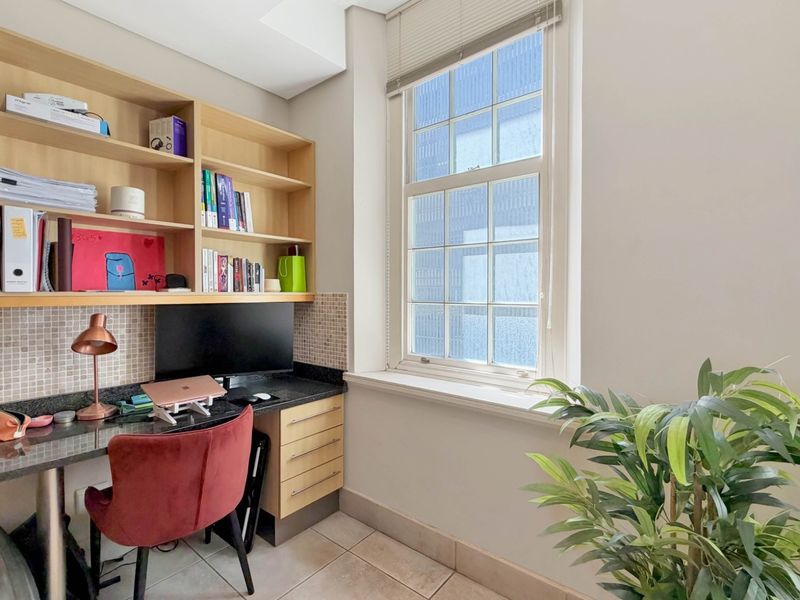 A functional home office featuring built-in desk cabinetry, integrated shelving, mosaic tile splashback, and a large sash window providing natural light.
