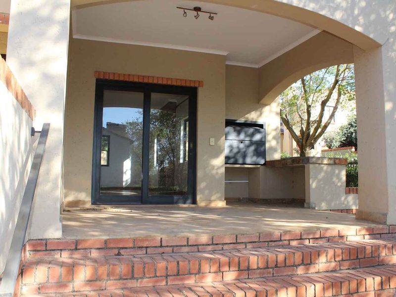 A covered patio area featuring a built-in braai, brick steps, and a sliding glass door providing access to the interior.