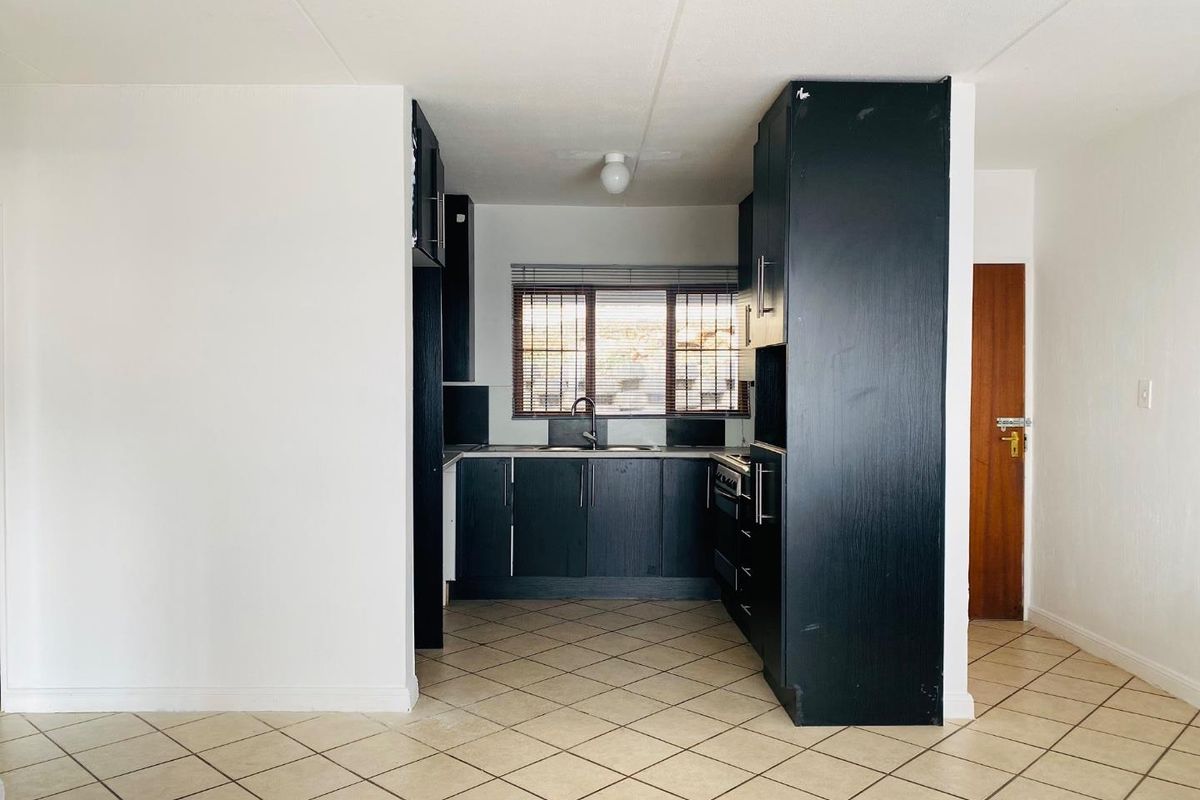 A functional kitchen featuring dark built-in cabinetry, tiled flooring, and a window with venetian blinds, offering a clean and practical layout.