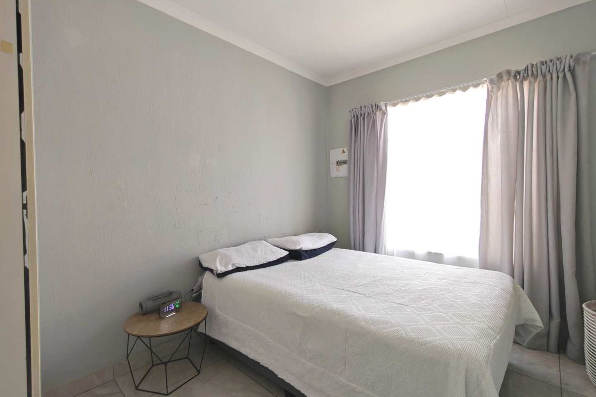 A functional bedroom featuring tiled flooring, neutral wall finishes, and a window with curtain tracks.