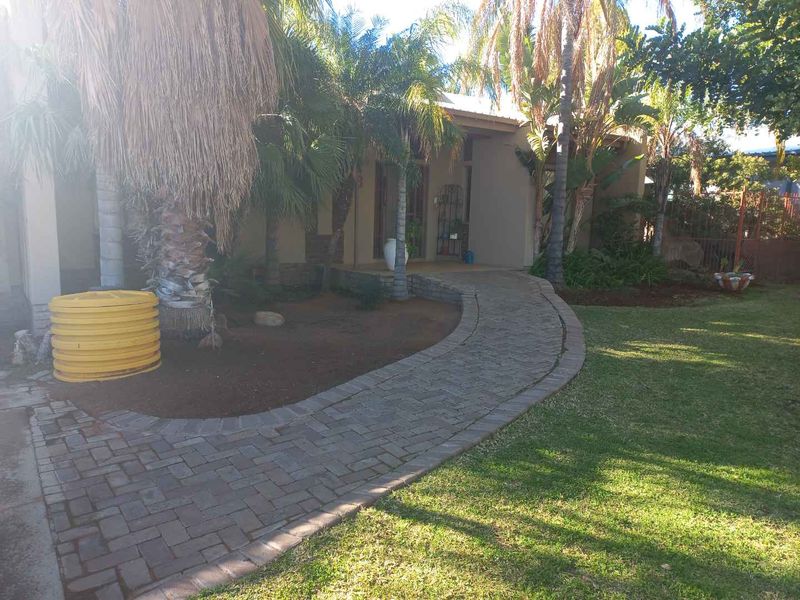 A welcoming front entrance featuring a paved walkway leading to a covered porch, surrounded by a well-maintained garden with mature palm trees.