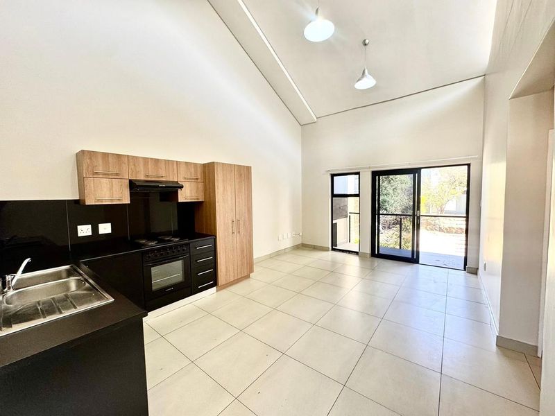 Spacious open-plan kitchen and living area featuring vaulted ceilings, modern cabinetry, tiled floors, and direct access to an outdoor patio through sliding glass doors.