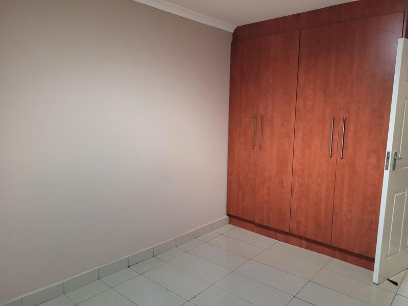 A clean, empty bedroom featuring neutral walls, tiled flooring, and ample built-in wooden cupboards.