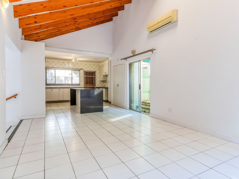 Spacious open-plan living and kitchen area featuring high vaulted ceilings with exposed timber beams, tiled flooring, and direct access to an outdoor space.