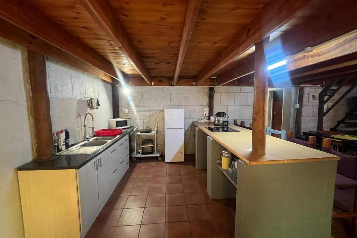 Rustic kitchen featuring exposed timber ceiling beams, tiled flooring, built-in cabinetry, and a breakfast bar with integrated cooktop.