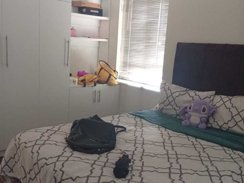 A bedroom featuring built-in white cupboards with integrated shelving and venetian blinds on the window.