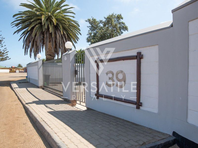 Street view of the property boundary wall featuring a metal gate, paved sidewalk, and exterior pillar lighting.