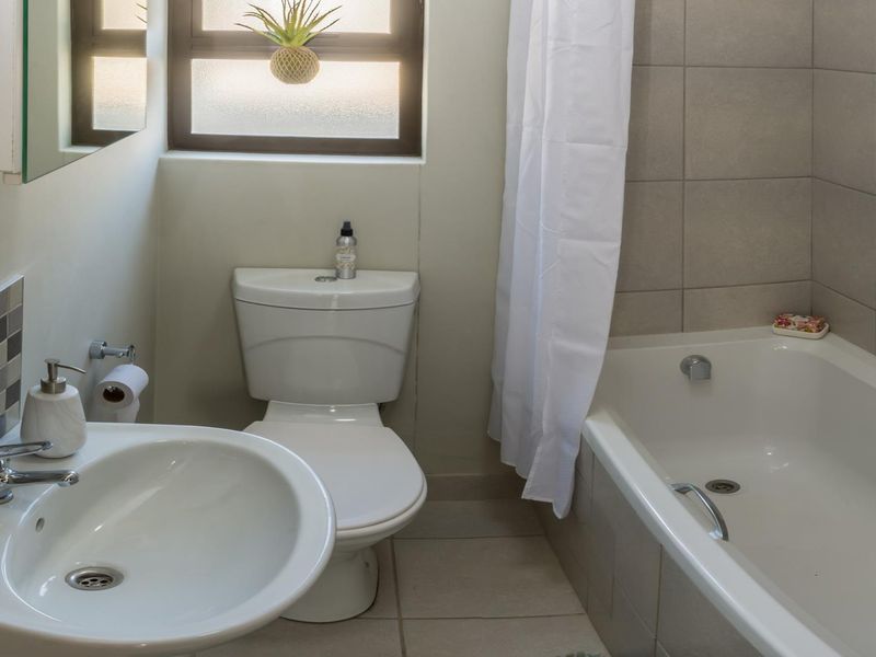 A functional bathroom featuring a pedestal basin, toilet, and a bathtub with tiled surround and splashback, complemented by natural light from the window.
