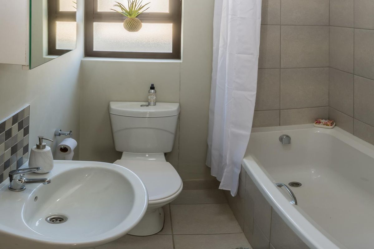A functional bathroom featuring a pedestal basin, toilet, and a bathtub with tiled surround and splashback, complemented by natural light from the window.