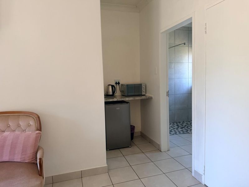 A compact kitchenette or scullery area featuring tiled flooring and a built-in countertop, with direct access to an adjacent bathroom.