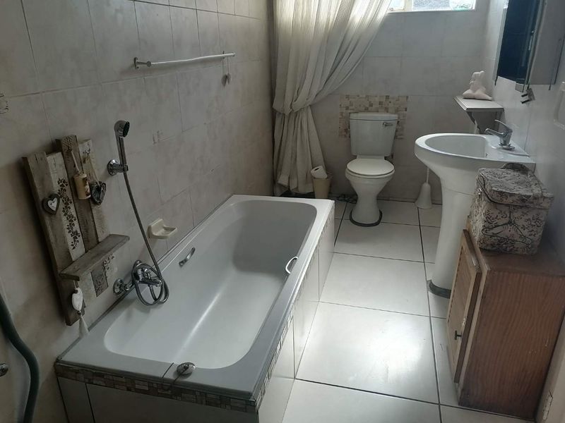 A functional bathroom featuring a bathtub, pedestal washbasin, and toilet with neutral wall and floor tiling throughout.