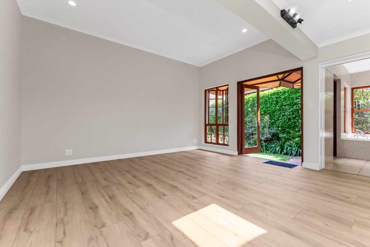 A bright, empty bedroom featuring modern laminate flooring, recessed lighting, and direct access to a private garden through wooden framed glass doors.
