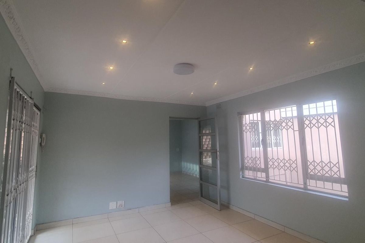 An empty living room featuring tiled flooring, recessed downlighting, decorative cornicing, and security bars on the windows and doors.