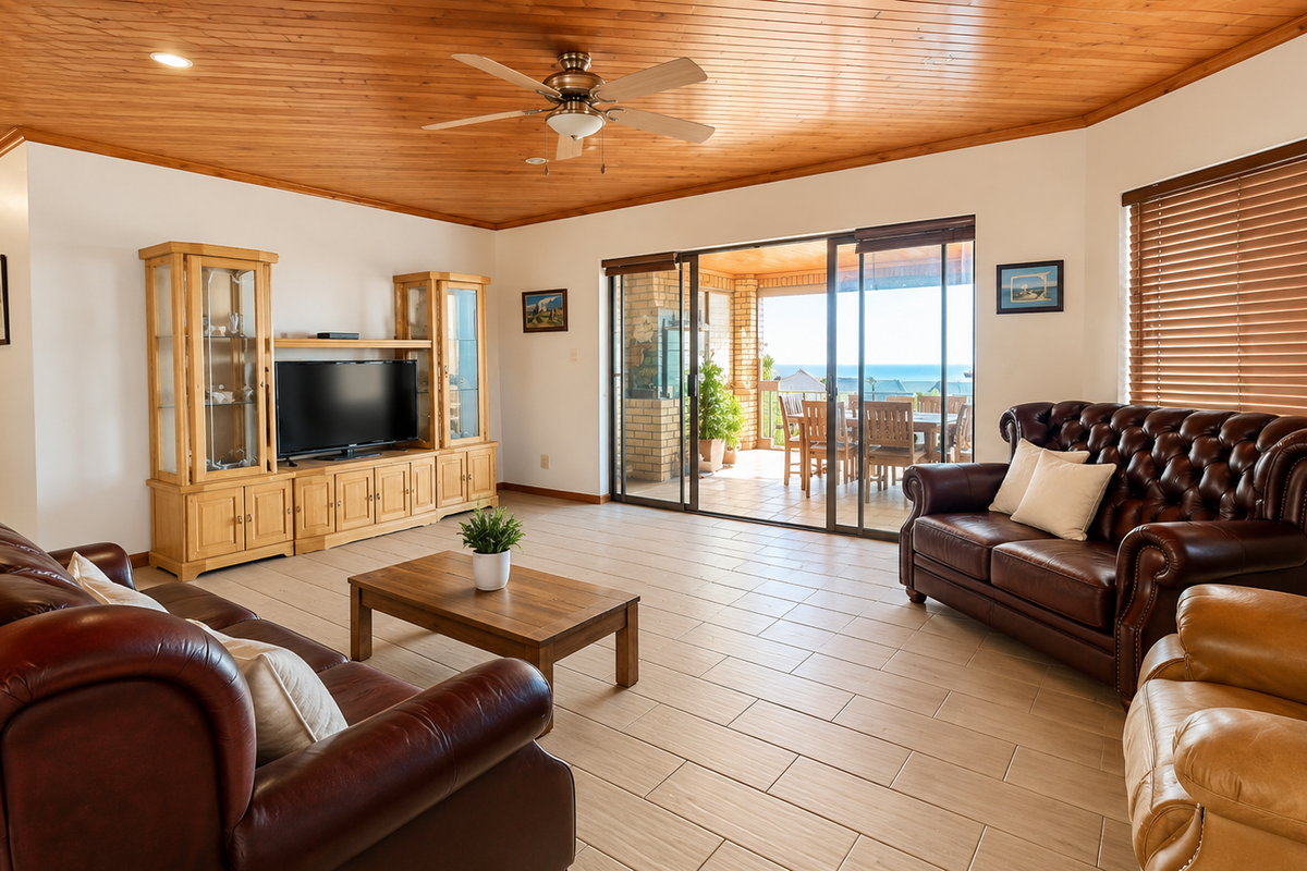 Spacious living room featuring a warm timber-clad ceiling, ceramic tiled flooring, and large sliding glass doors that open onto a covered patio with ocean views.