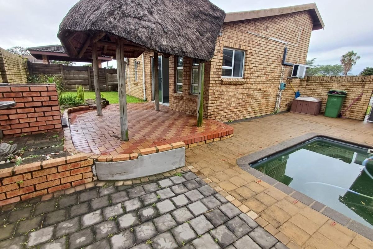 Rear exterior view featuring a thatched lapa, brick-paved patio area, and a swimming pool set against a facebrick townhouse facade.
