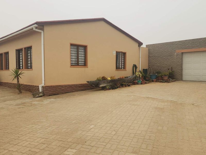 A single-story residential property featuring a paved driveway, attached garage, and neutral exterior wall finish with security bars on the windows.