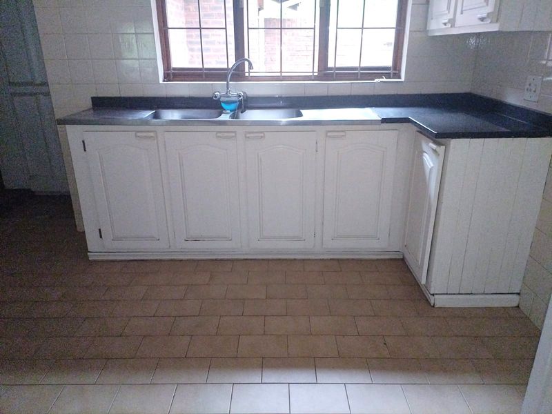 A functional kitchen area featuring built-in white cabinetry, a stainless steel double sink, and tiled flooring, offering a blank canvas for modern updates.