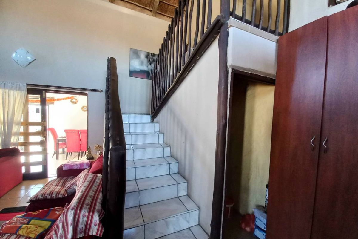 Interior view of a living area featuring a tiled staircase with a rustic timber balustrade and a thatched roof ceiling.