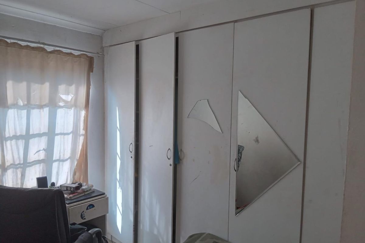 A bedroom featuring built-in wardrobes with damaged mirror panels and signs of wear on the wall finishes.