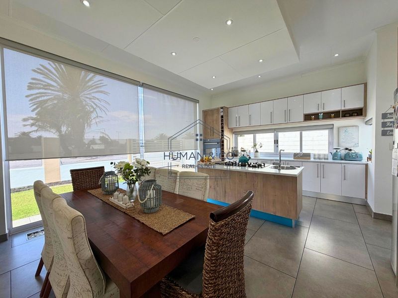 Modern open-plan kitchen and dining area featuring a central island, gas hob, built-in oven, and large windows with roller blinds.