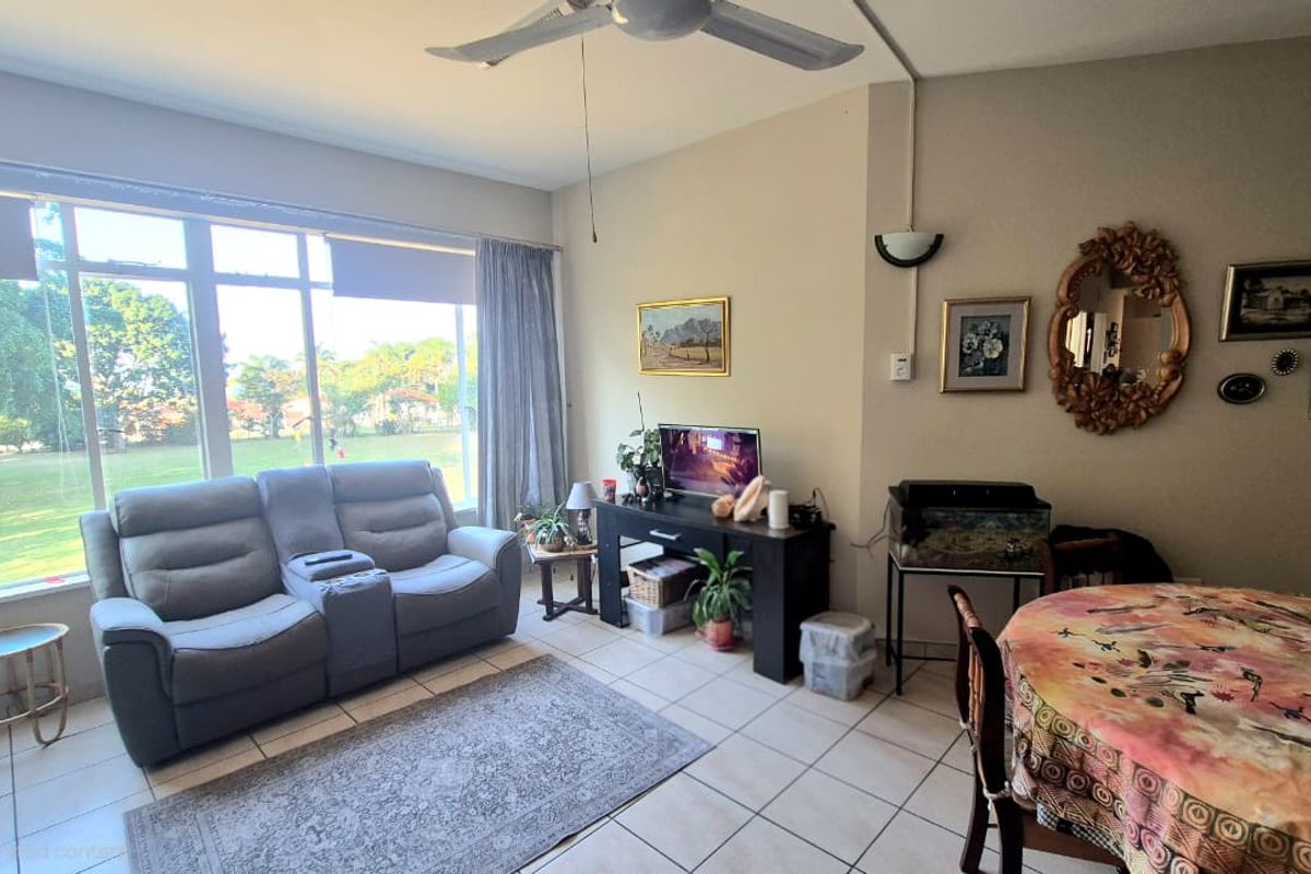 A bright living room featuring tiled flooring, a ceiling fan, and a large window providing natural light and garden views.
