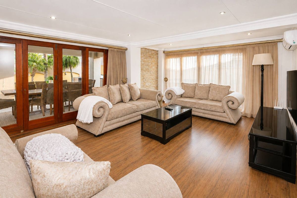 Spacious living room featuring laminate flooring, a stone feature wall, recessed lighting, and timber-framed sliding doors providing seamless access to the outdoor patio area.