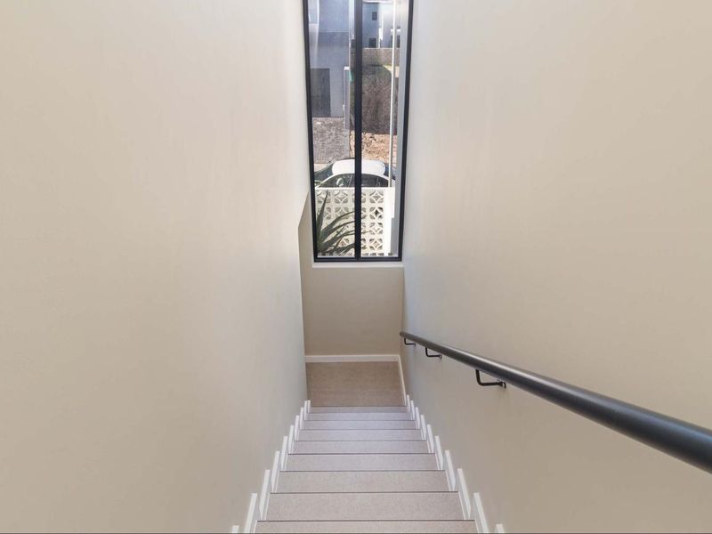 A clean, modern staircase featuring a sleek black handrail and a tall, narrow window that provides natural light to the hallway.