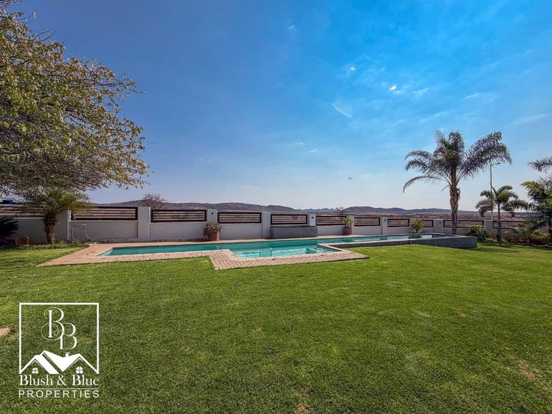 A well-maintained outdoor pool area featuring a swimming pool with brick coping, surrounded by a manicured lawn and secure perimeter boundary wall.