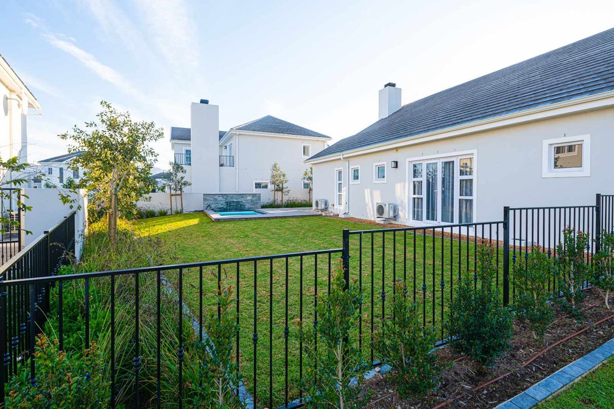A well-maintained rear garden featuring a manicured lawn, a small plunge pool with a stone water feature, and modern exterior building finishes.